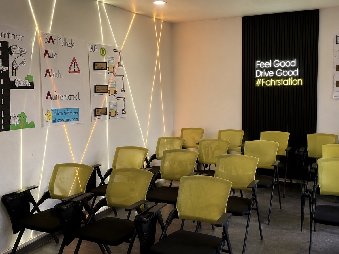 Moderner Theorieraum der Fahrstation mit Neon-Schriftzug 'Feel Good Drive Good' und Sitzplätzen für den Unterricht